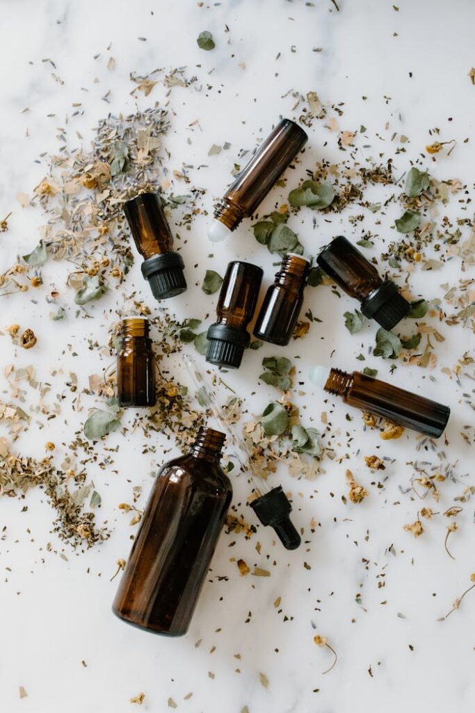 Flatlay of essential oil bottles surrounded by dried herbs on a white background.